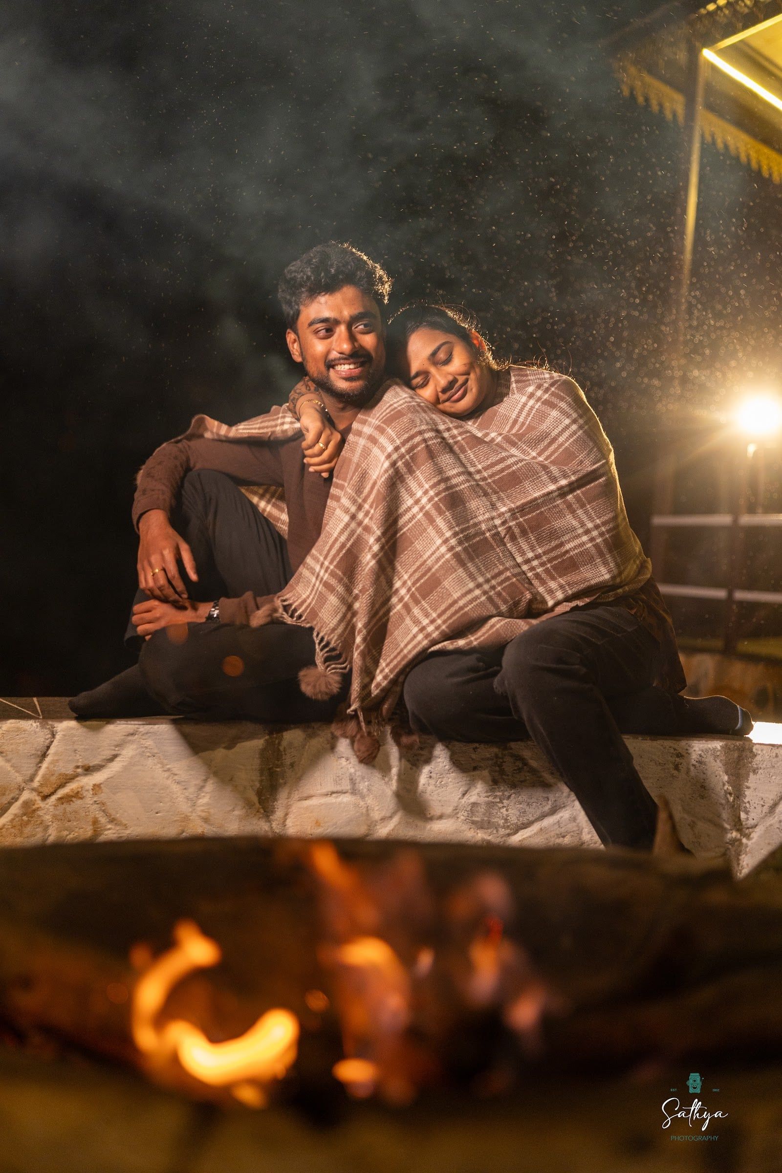 Couple wrapped in a shawl beside a bonfire at night