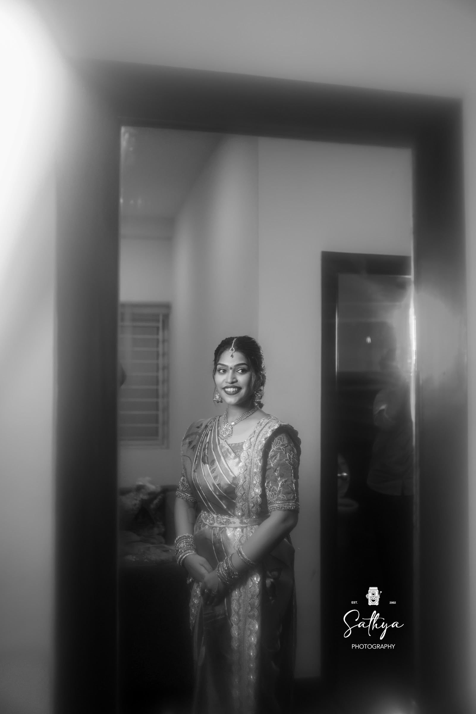 Black-and-white frame of a bride in a silk saree standing in a doorway