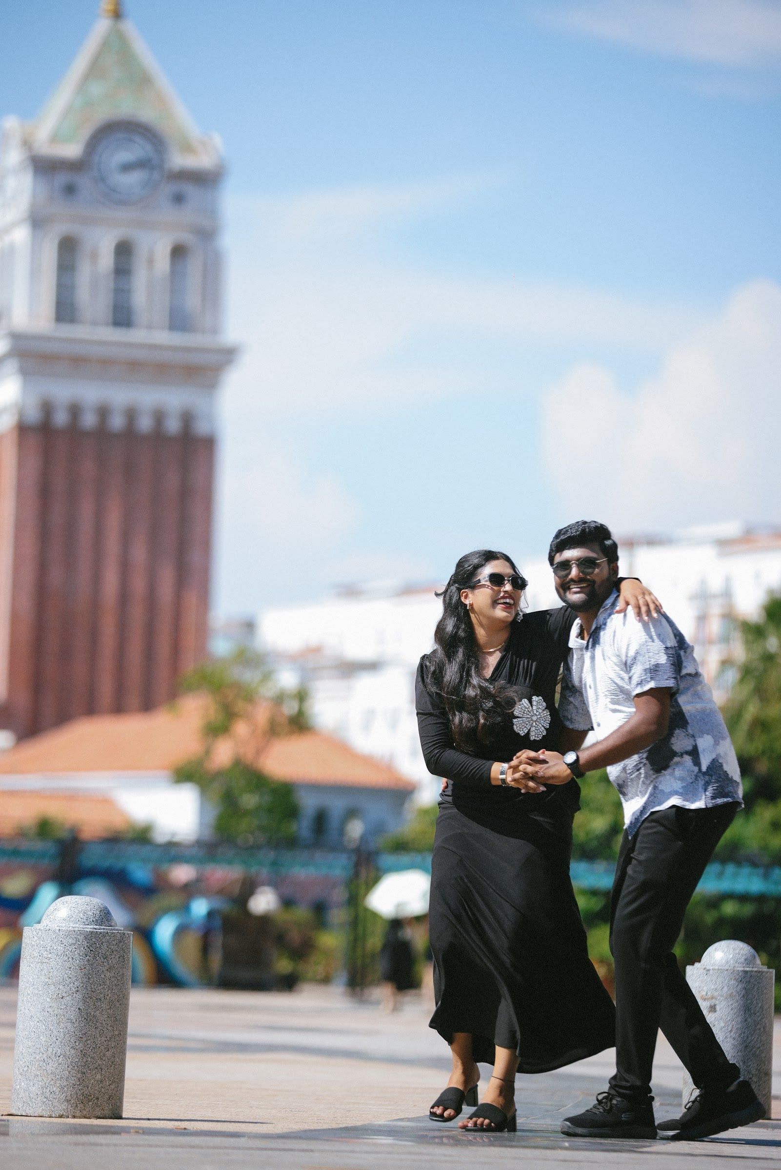 Couple laughing in front of a clocktower on a bright day