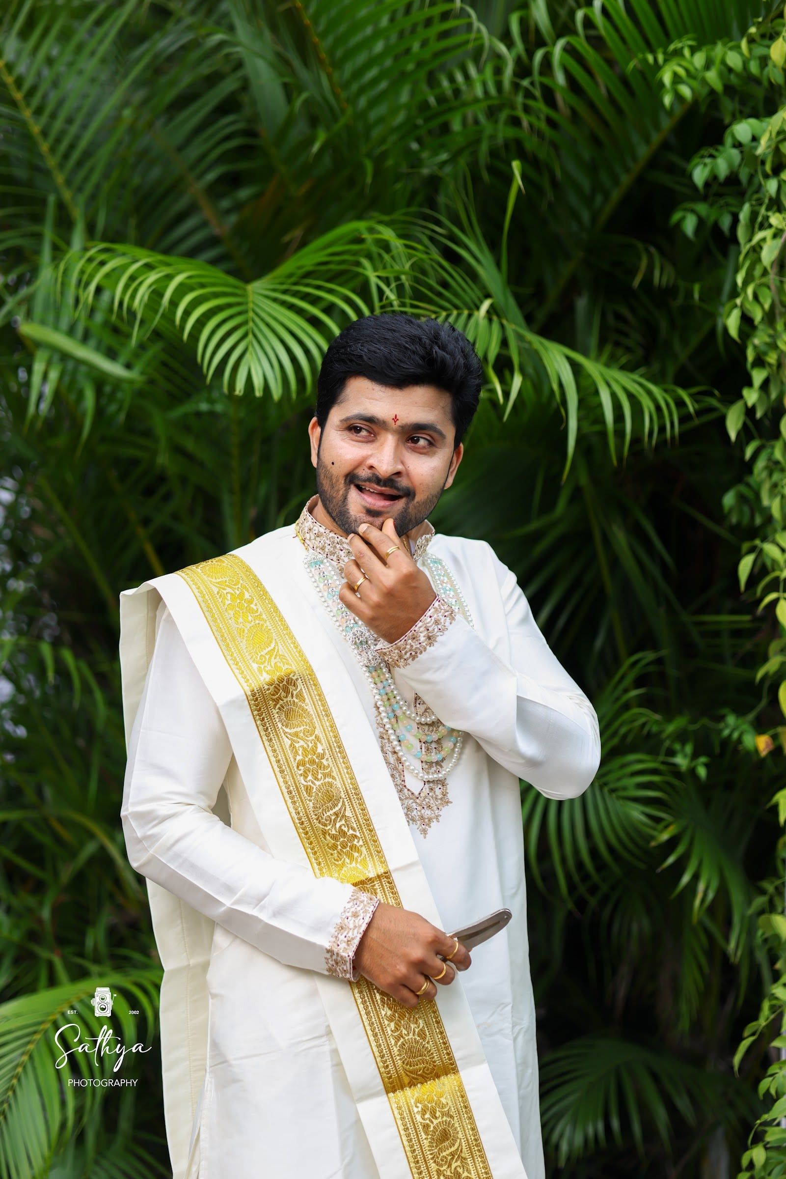 Groom in a cream kurta and gold kanduva among palms