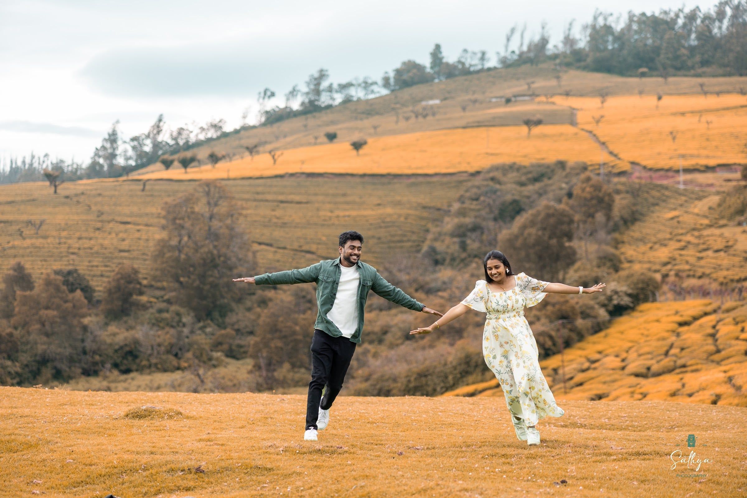 Couple running with arms wide across golden hills