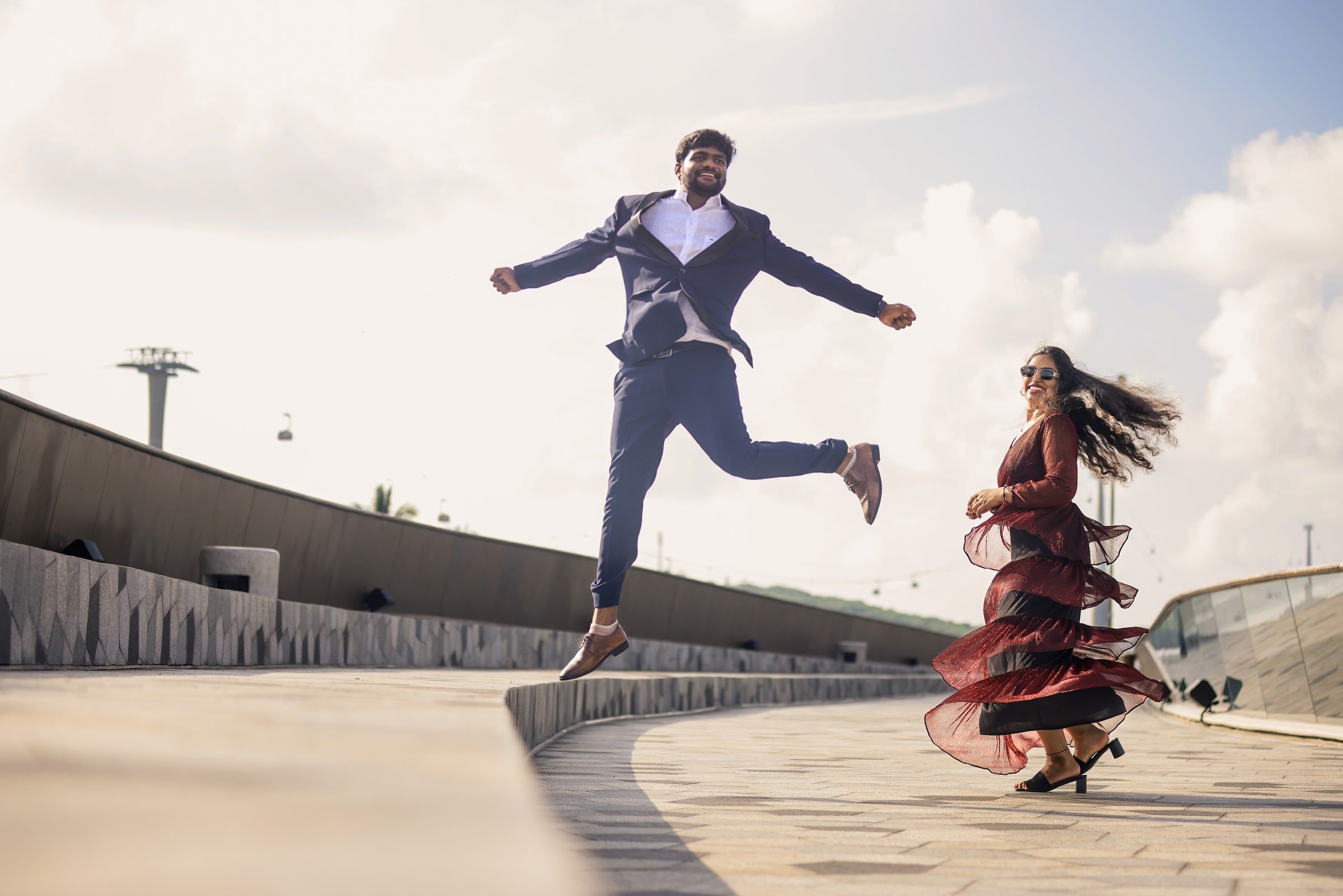 Groom leaping mid-air as the bride twirls on a waterfront promenade
