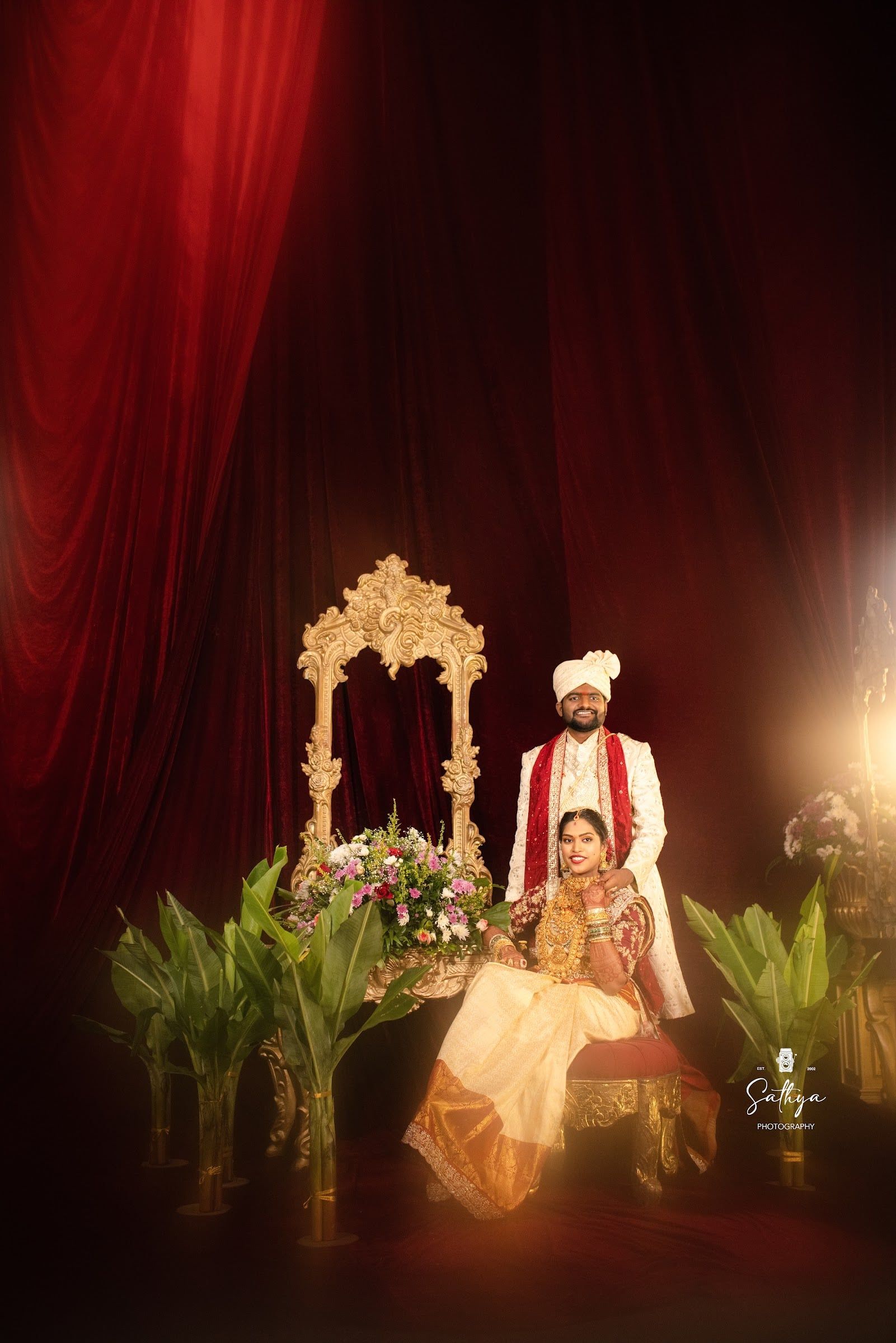 Bride and groom seated on a gilded throne before red drapes
