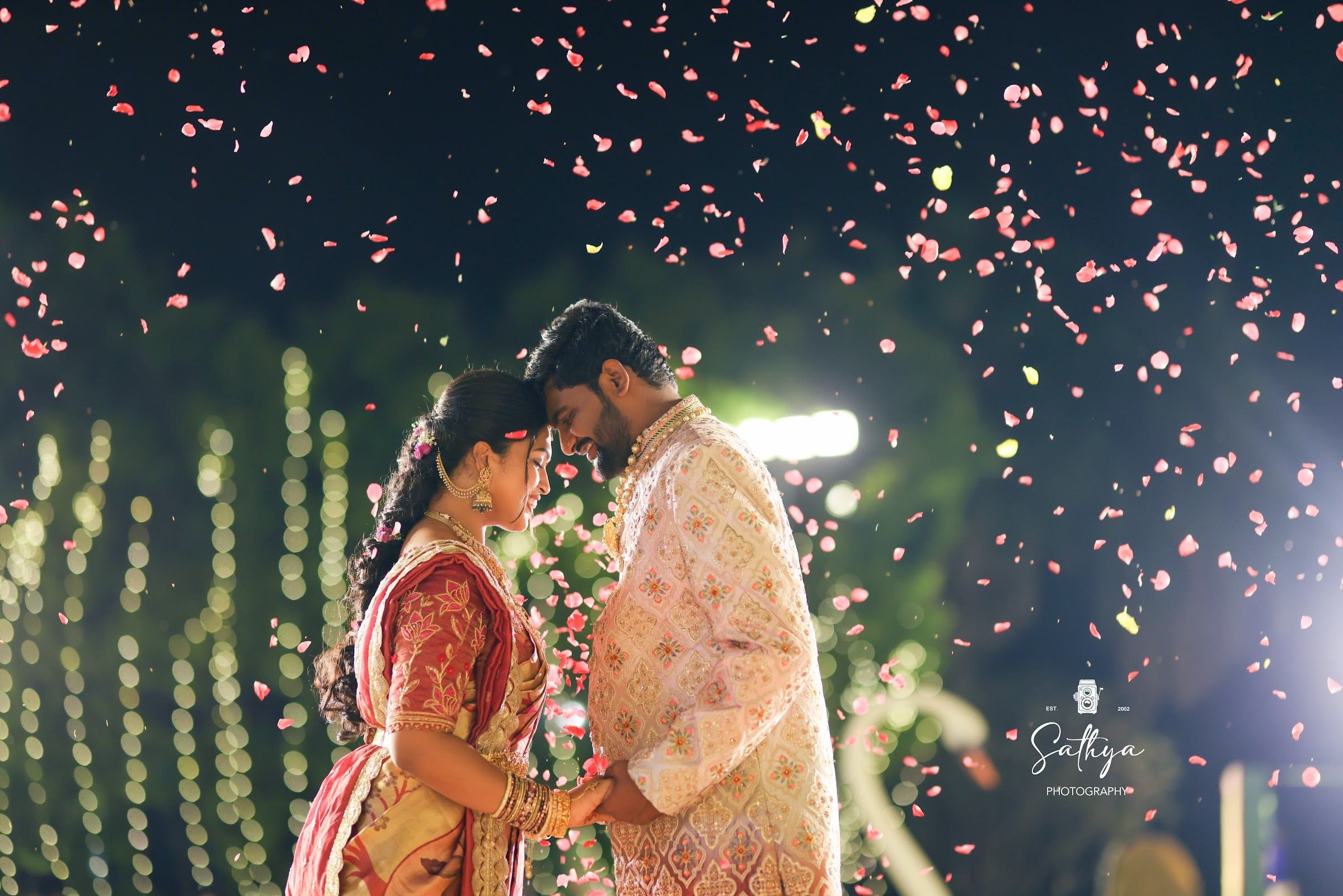 Couple forehead to forehead as rose petals rain down at night