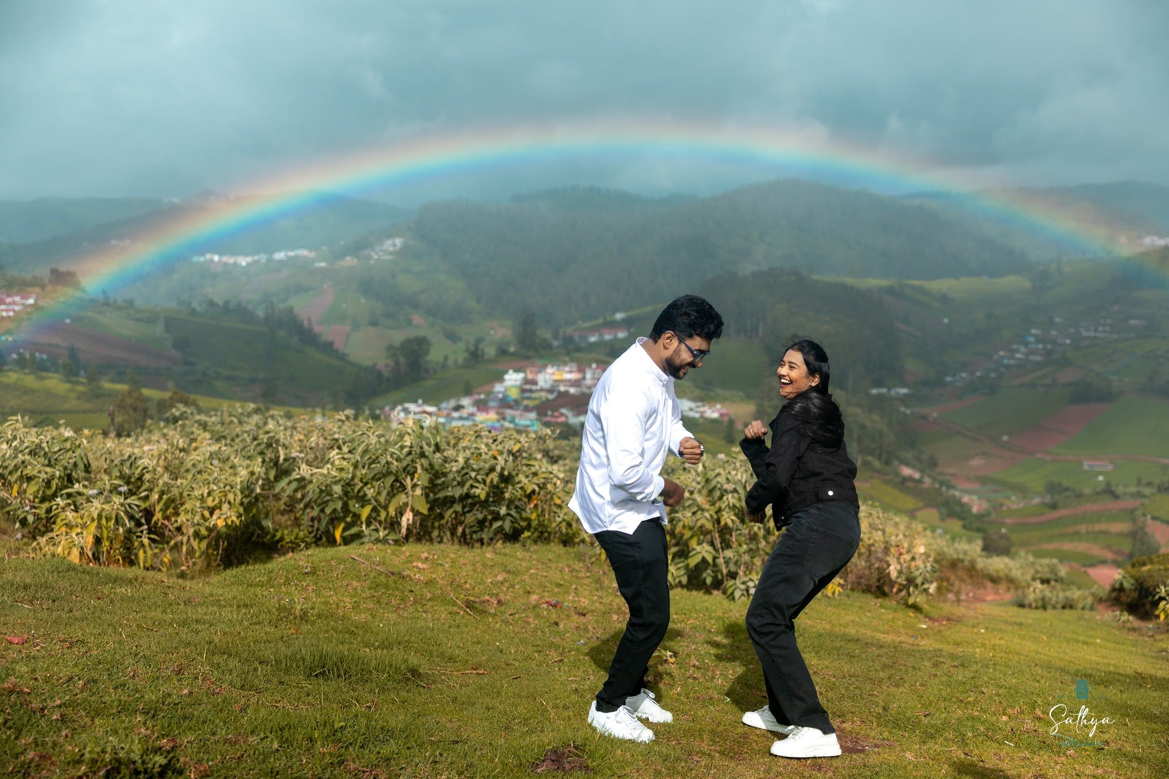 Couple dancing on a hilltop beneath a rainbow