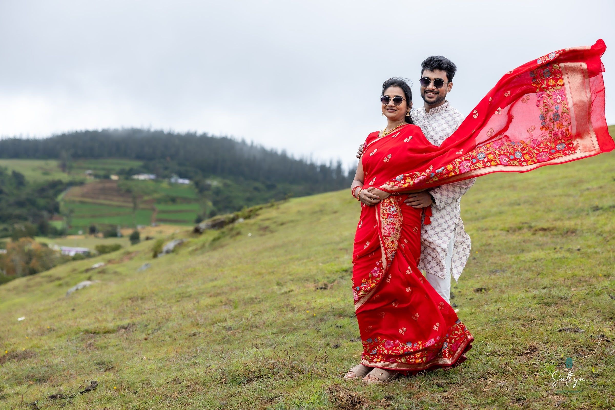 Bride’s red saree pallu flying in the wind on a green hillside