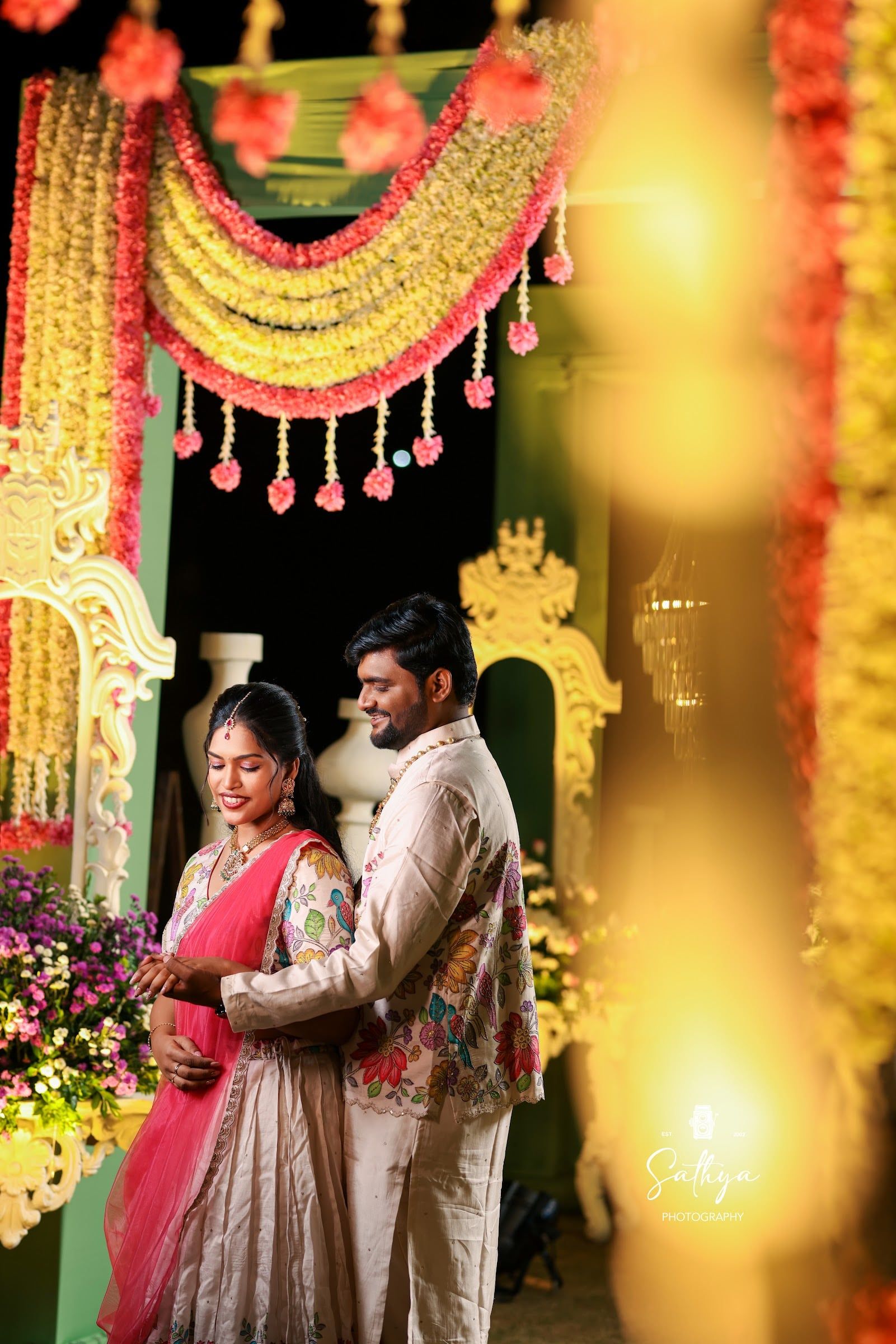 Couple beneath a marigold and floral arch at their sangeet night