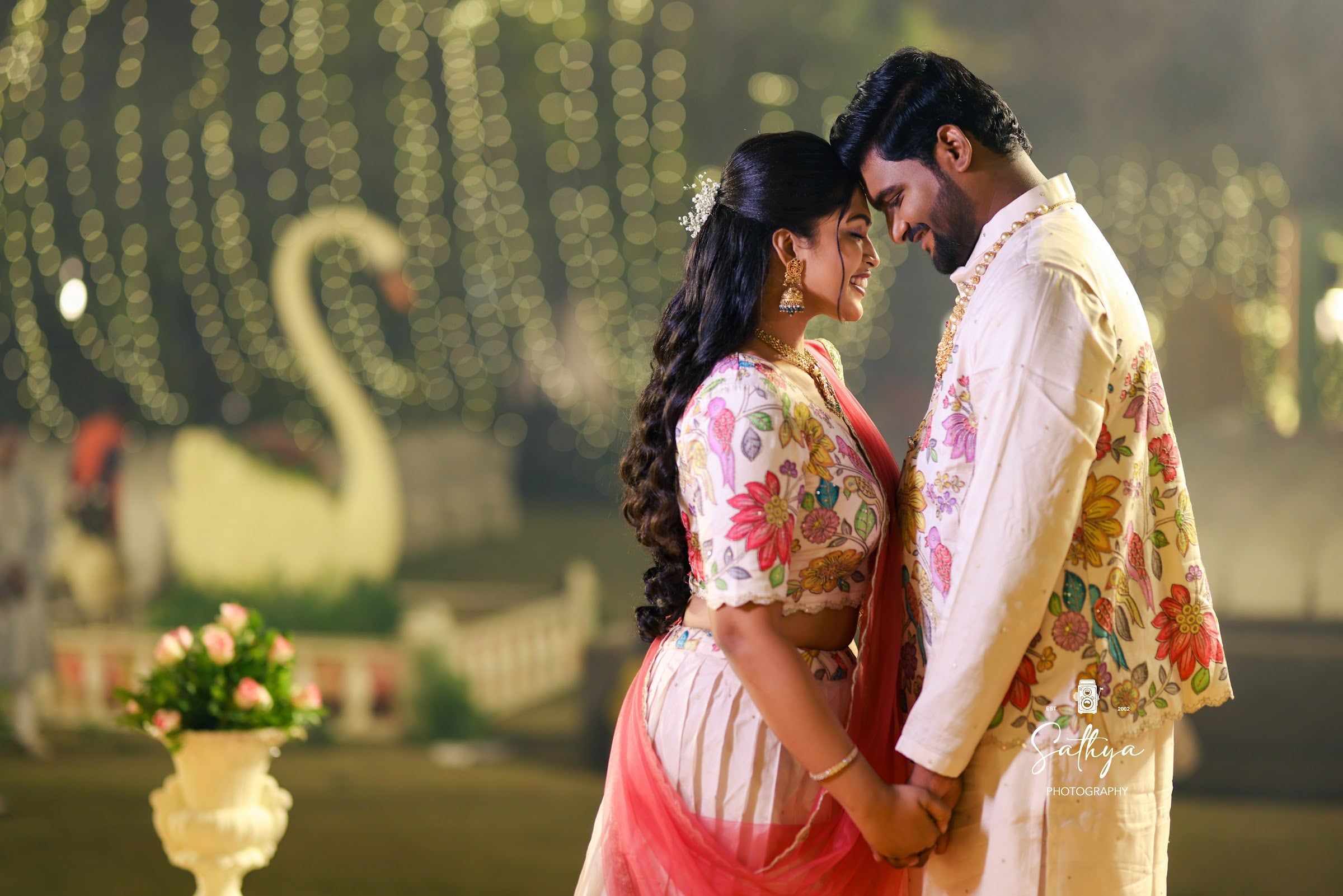 Bride and groom forehead to forehead among fairy lights at a sangeet