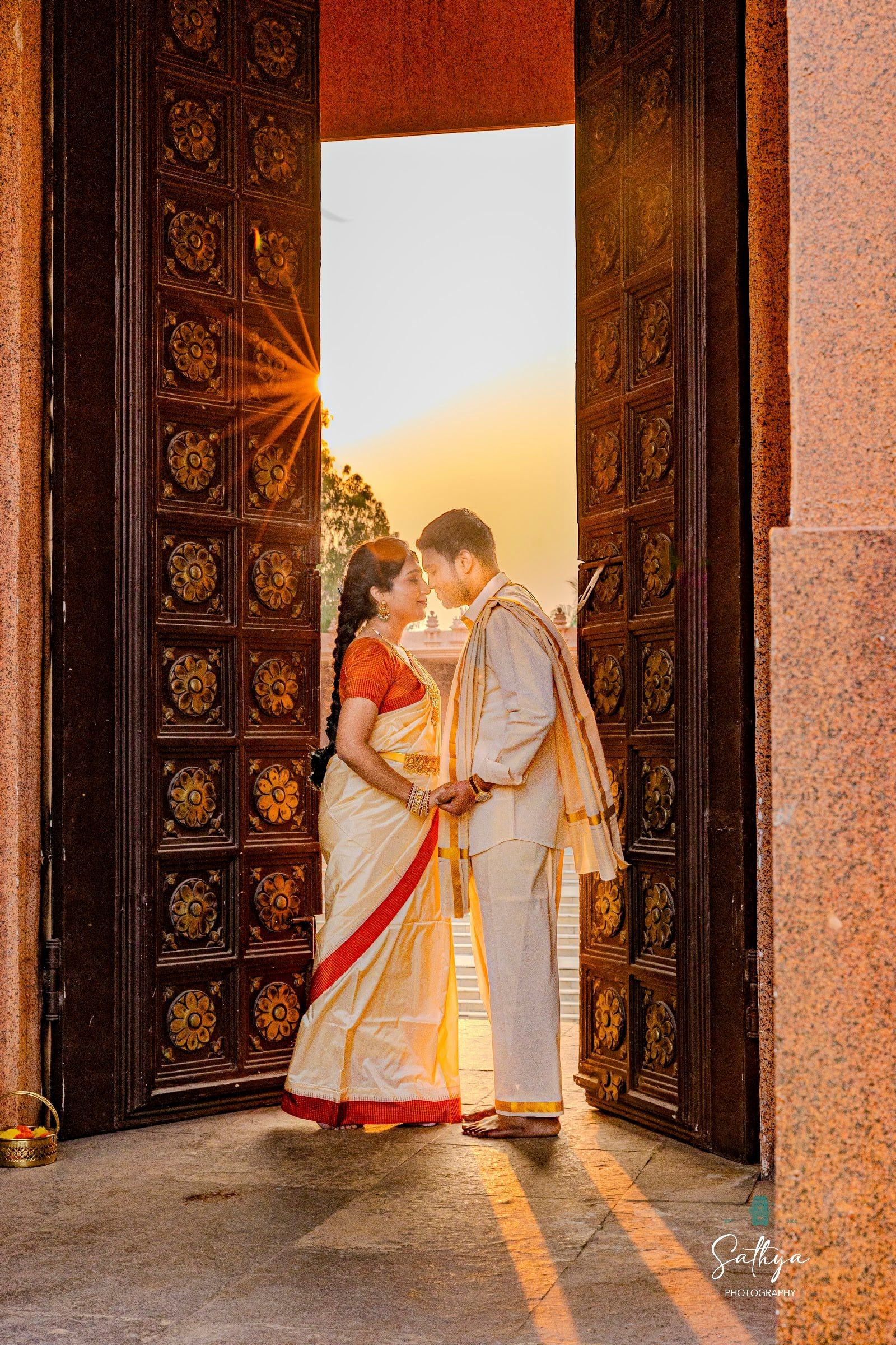 Bride and groom in a carved temple doorway with the sun behind them