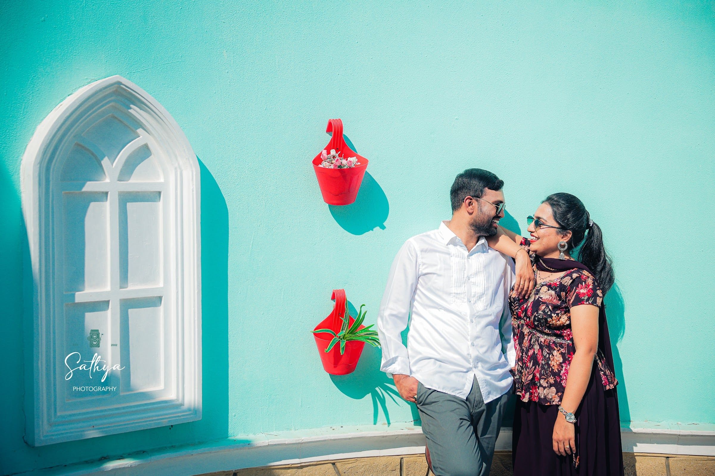 Couple laughing against a turquoise wall with red flower pots